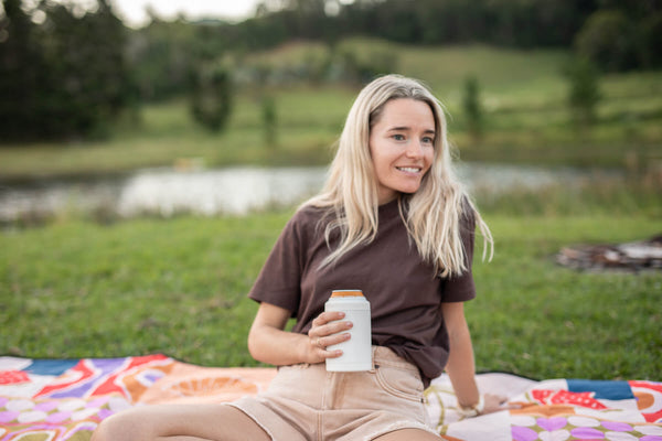 Woman holding white can cooler with orange band on picnic blanket by water