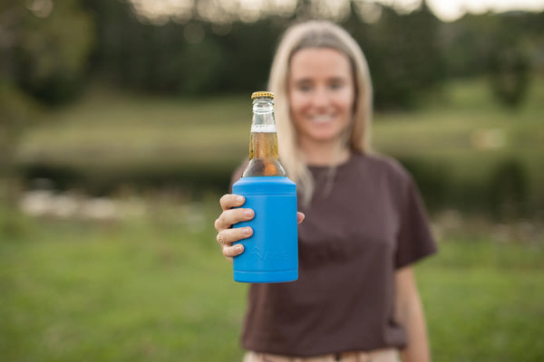 Blue neoprene bottle cooler holding a beer bottle, displayed by woman in outdoor garden setting