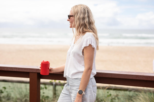 Campfire Red coffee cup lid shown on beverage container held by woman at beach