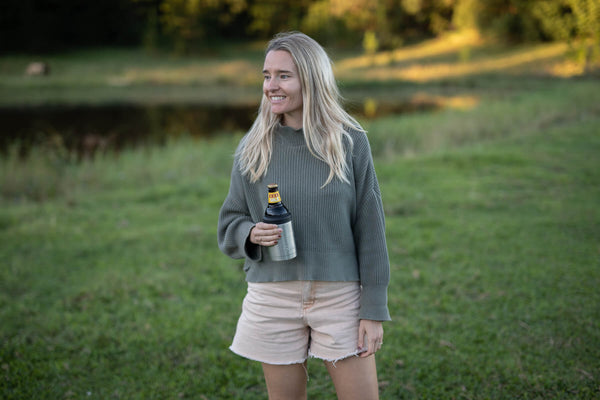 Classic Silver cooler and coffee cup in use, held by woman wearing gray ribbed sweater and cream shorts outdoors