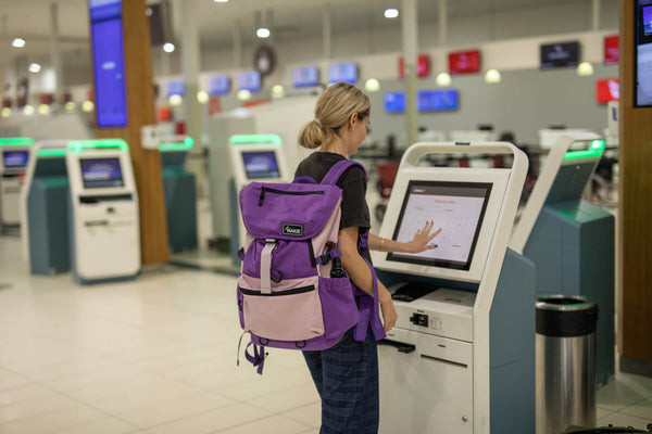 Purple and pink recycled travel backpack with padded straps worn at airport check-in kiosk