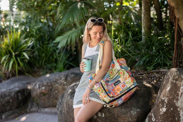 Retro Shores recycled tote bag with colorful beach-themed print, carried by woman in outdoor garden setting.