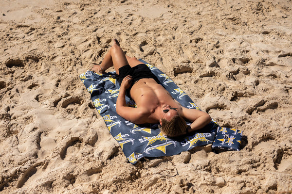 Navy Cowboys NRL beach towel with yellow logo print, laid on sand with person resting on it