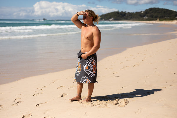 Black board shorts with white and orange tiger graphic print, worn on beach