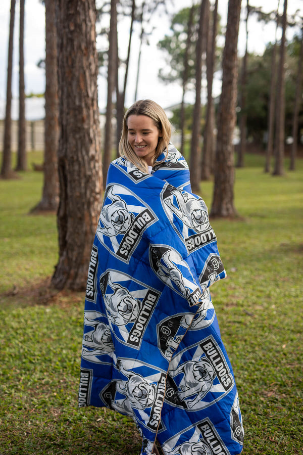 Blue and white Bulldogs NRL puffy blanket with dog logo print, worn as wrap by woman outdoors among trees