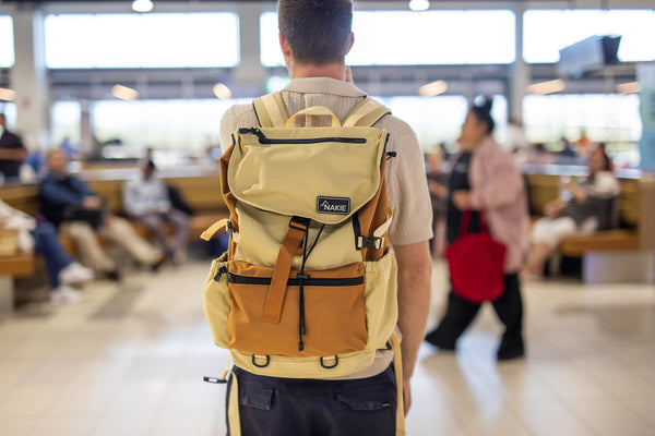 Sahara Sand recycled travel backpack with tan and caramel colorblock, flap closure, and tan straps, worn on back.