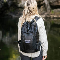 Women wearing a black backpack with 'Nakie' branding overlooking a waterfall