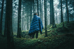 Man nestled amidst the tranquil woods, wrapped in a Nakie puffy blanket, enjoying warmth and comfort during an outdoor adventure in nature preview #4