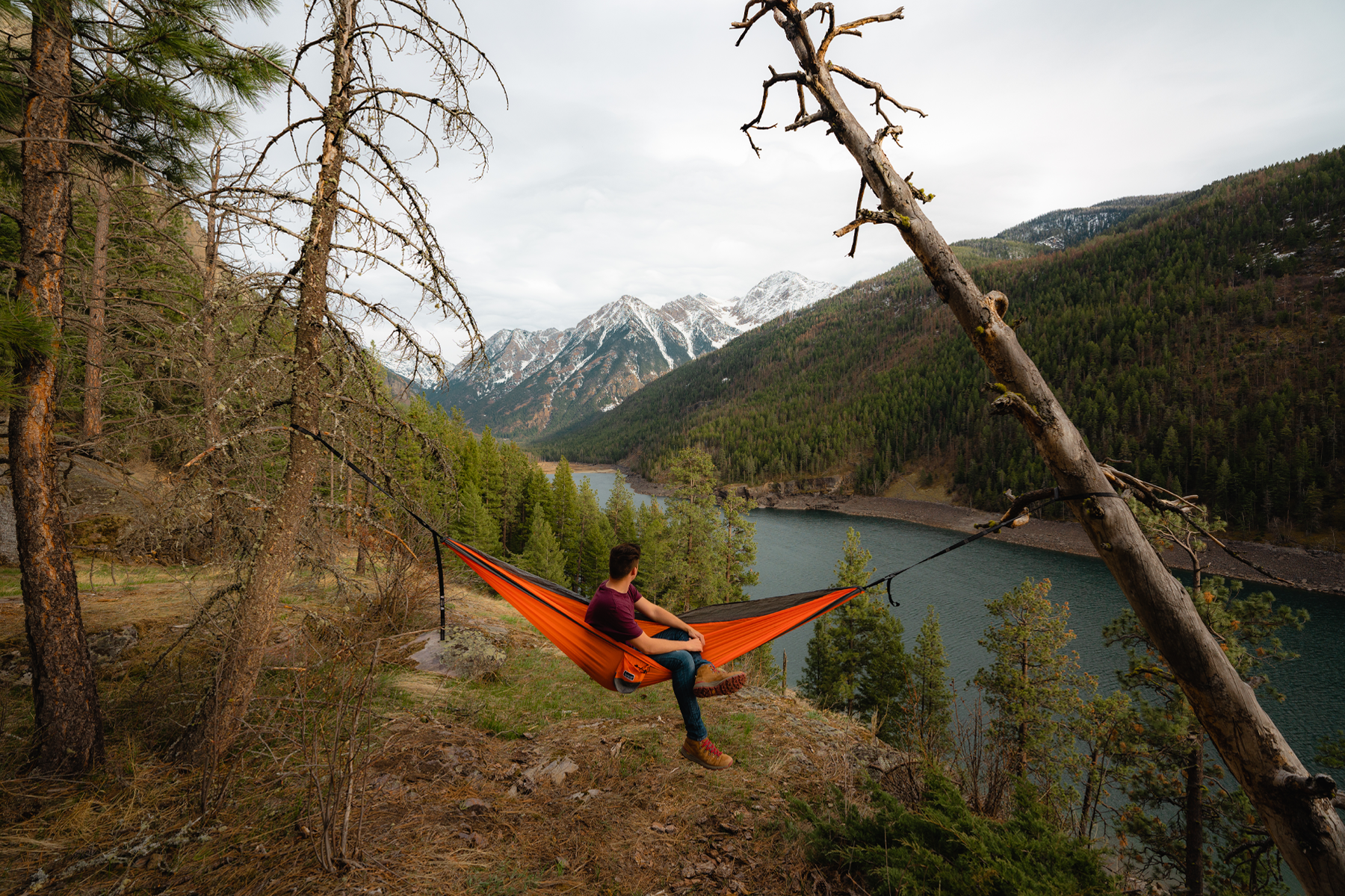 Person relaxing in a Nakie Sunburnt Orange Hammock overlooking a mountain lake.