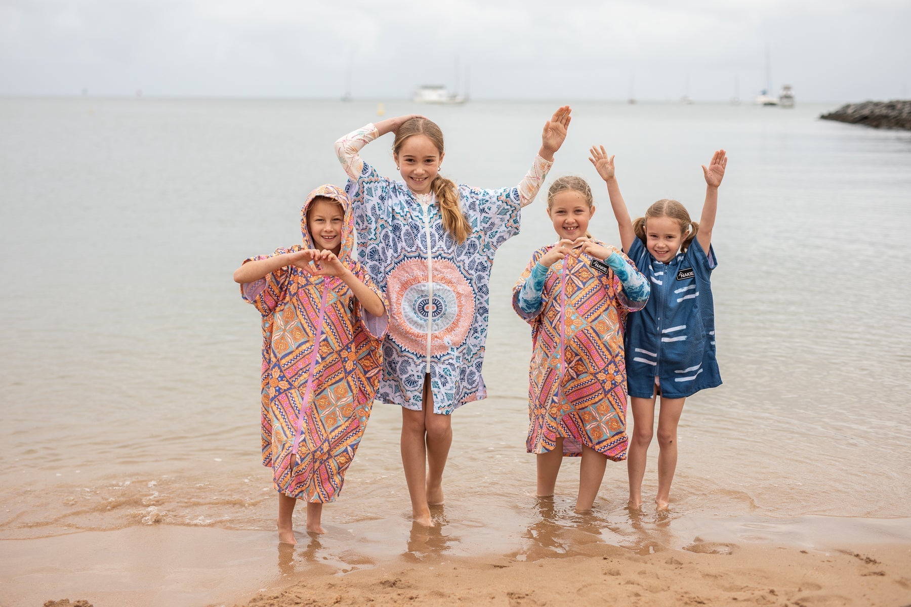Kids posing playfully in Nakie hooded towels on the beach.