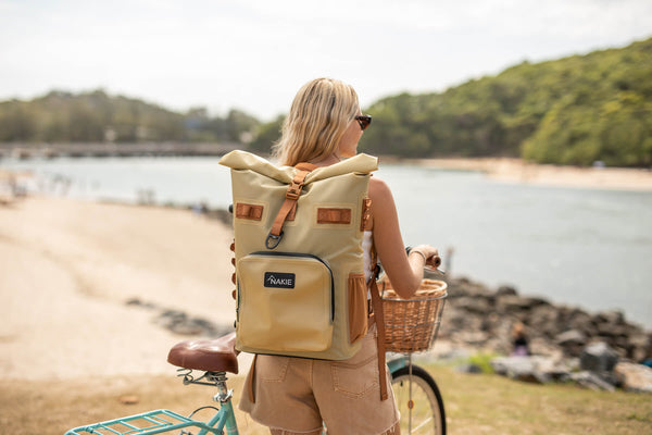 Sahara Sand recycled cooler backpack with roll-top closure and brown leather accents, worn on wearer's back at beach