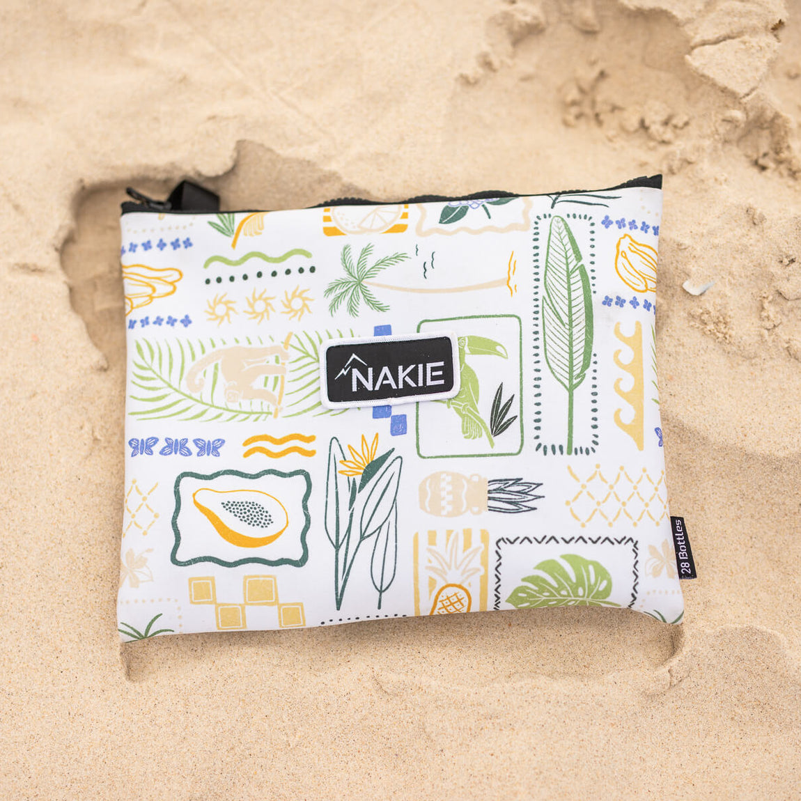 NAKIE Toucan Bay recycled sand-free beach towel with tropical botanical print in white, yellow, and blue on sand.
