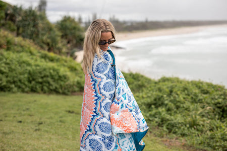 Sustainable down puffy blanket with blue, coral, and white geometric pattern, draped over shoulder outdoors.