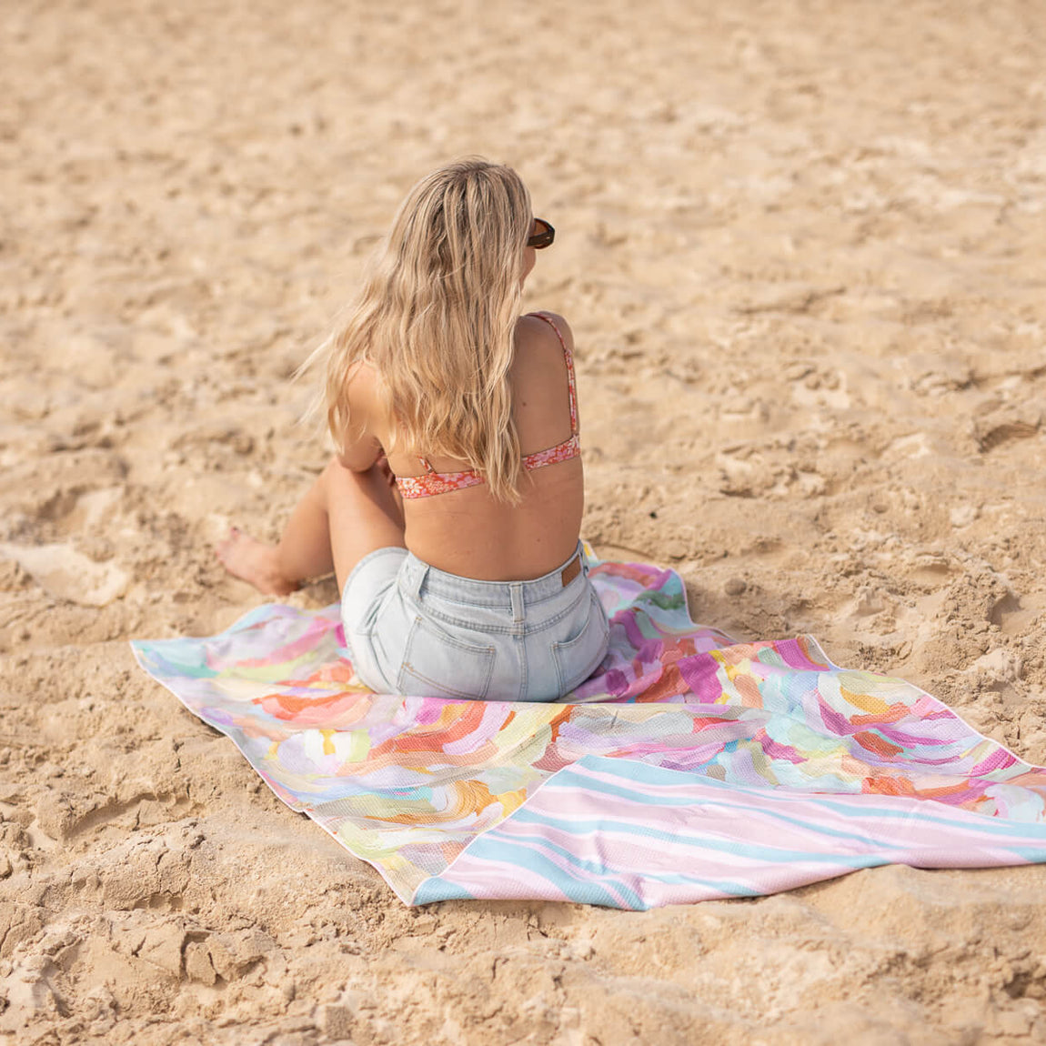 Recycled sand-free beach towel with colorful watercolor and striped pattern, displayed on sand.