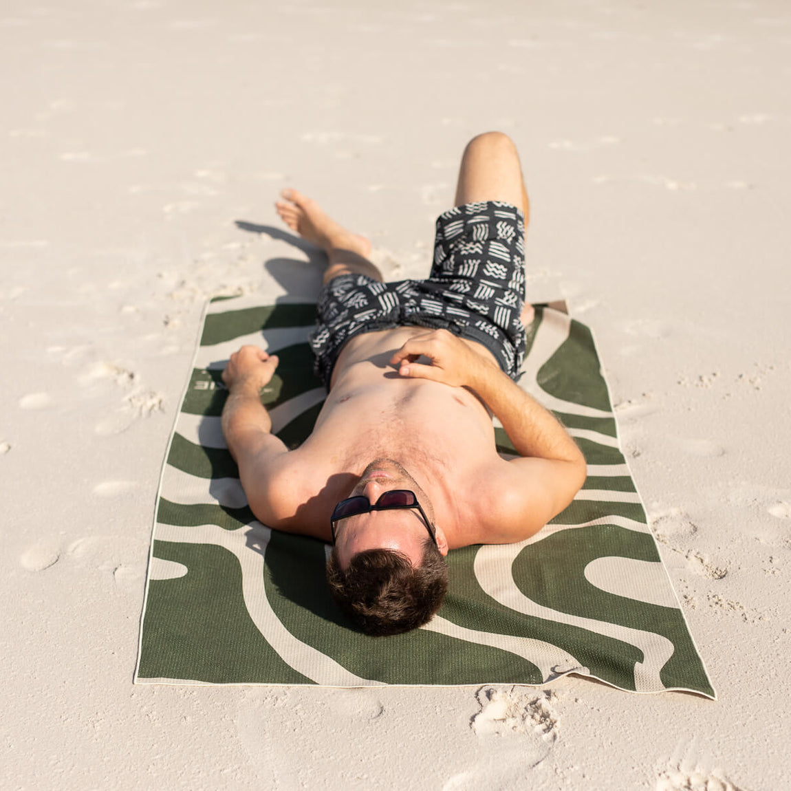 Eucalyptus green and white patterned recycled beach towel with man lying on sand at beach