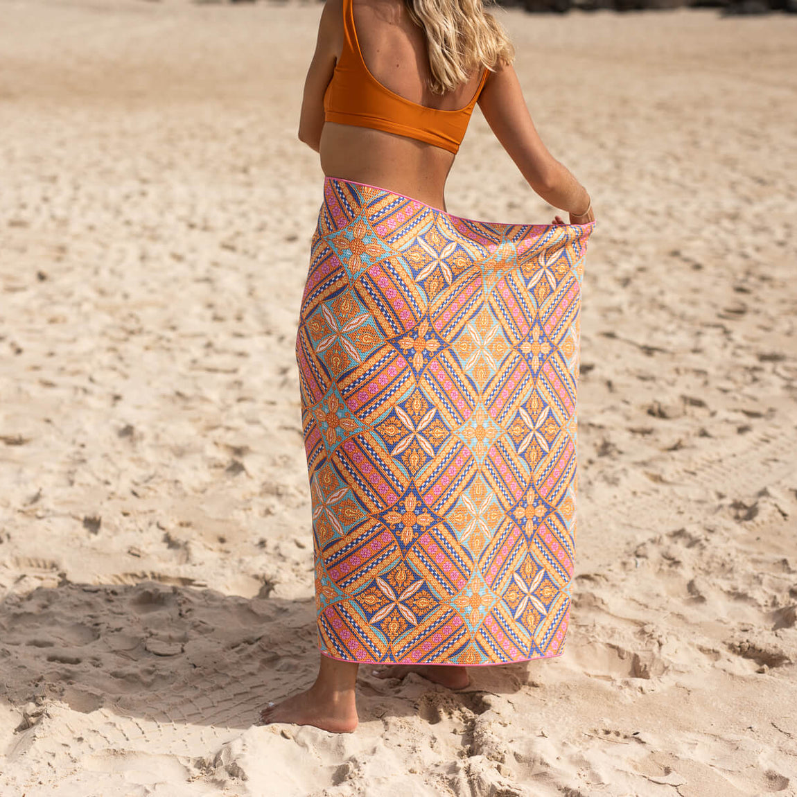 Multicolored geometric patterned beach towel in orange, pink, blue and yellow, worn as a wrap on sandy beach