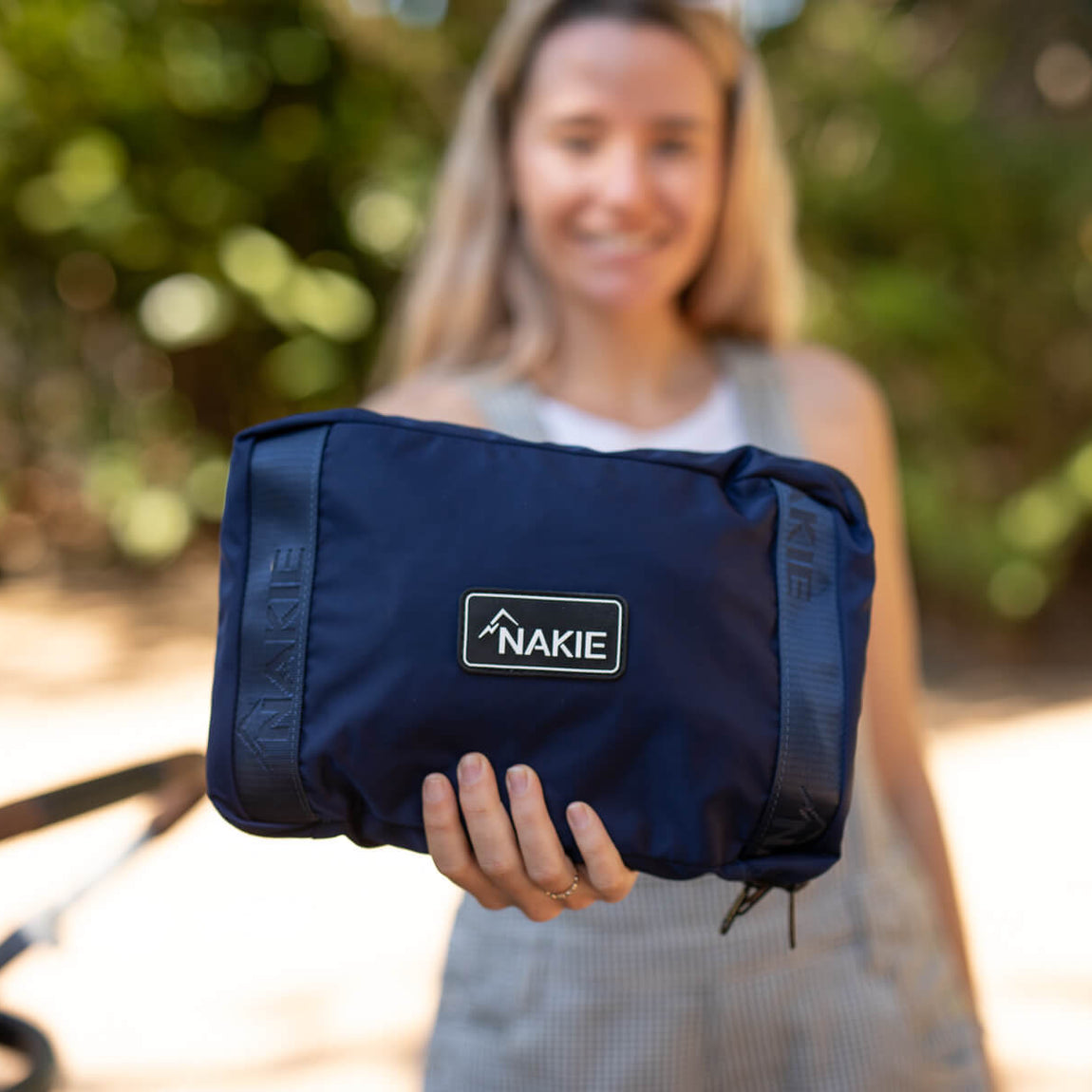 Navy recycled tote bag with NAKIE logo patch, held in hand outdoors