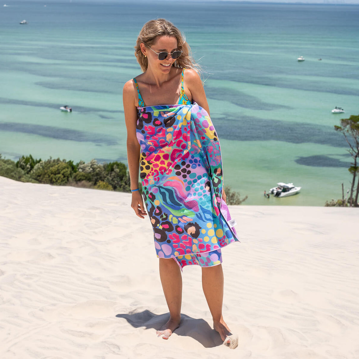 Colorful abstract patterned beach towel wrap in pink, blue, and yellow tones worn at the beach