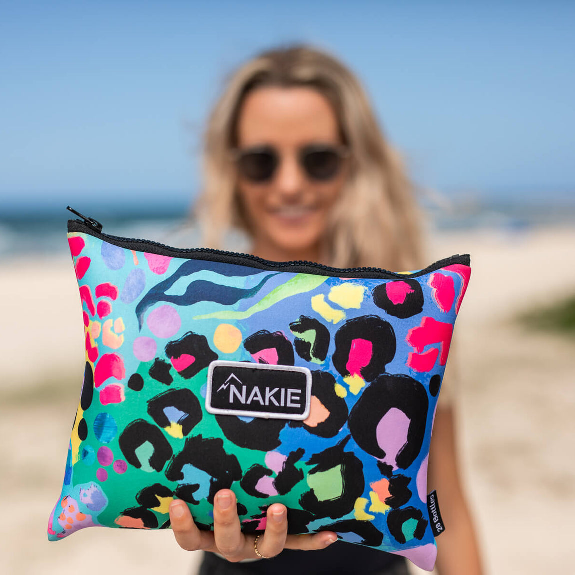 Colorful sand-free beach towel with leopard print and rainbow geometric pattern, rolled and held up at the beach