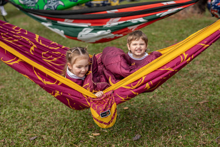 Two children in a colorful hammock on grass