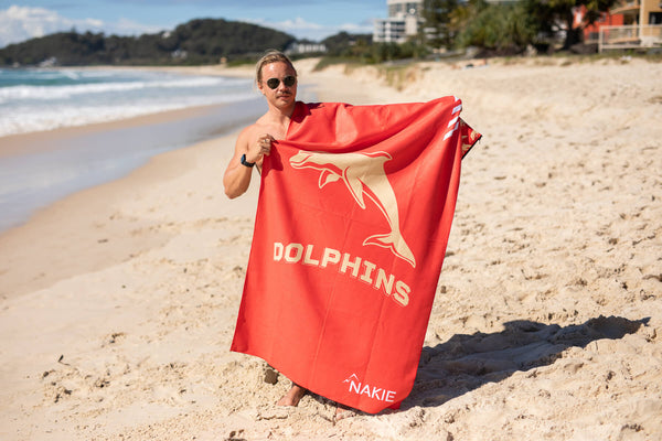 Red recycled sand-free beach towel with gold dolphin graphic and "DOLPHINS" text, displayed on beach