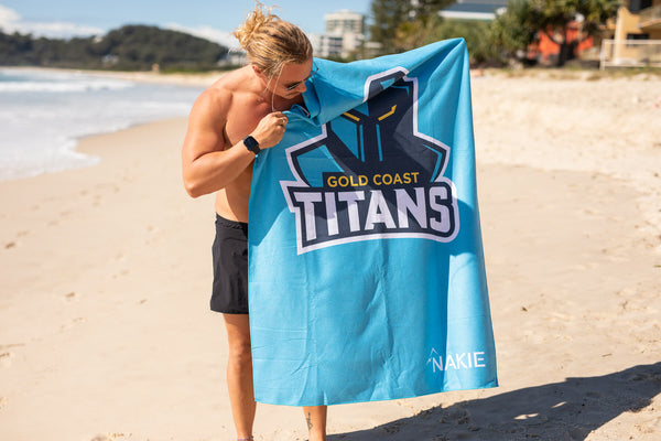 Gold Coast Titans bright blue beach towel with team logo and Nakie branding, sand-free texture, displayed on beach