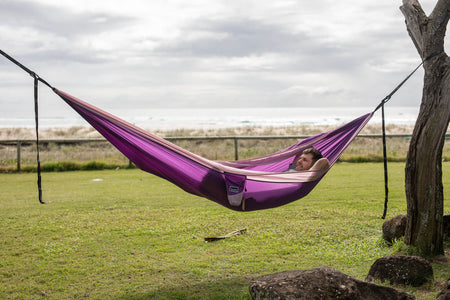 A calming image of a purple Nakie hammock elegantly stretched between two trees, providing a sustainable oasis for rest and rejuvenation