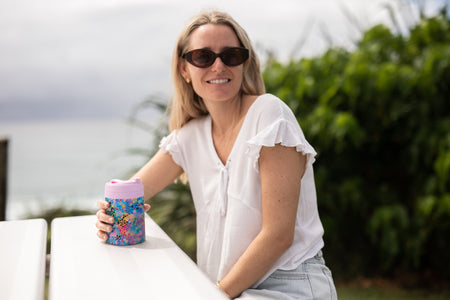 Woman smiling with a Kasey Rainbow Cooler & Coffee Cup at a picnic table